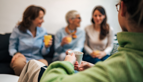 Four women gathered together, drinking coffee and smiling